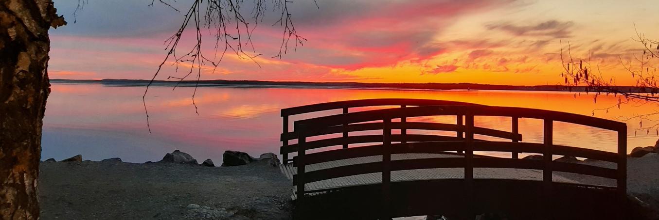 Pieni puinen silta Näsijärven rannalla, taustalla auringonlaskun punertama taivas.